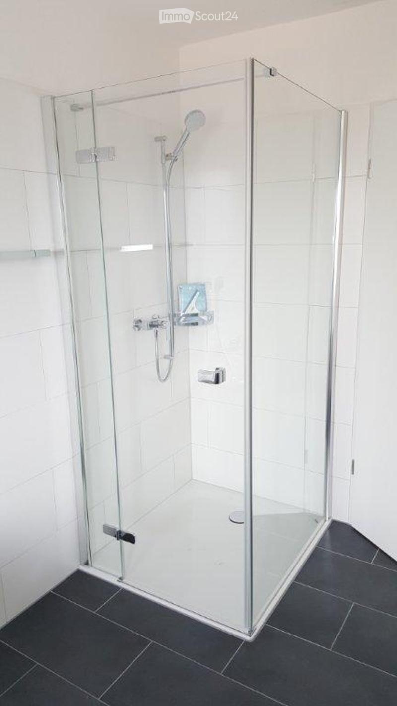 Modern bathroom with a glass-enclosed shower stall, white tiles, and a dark grey tiled floor.