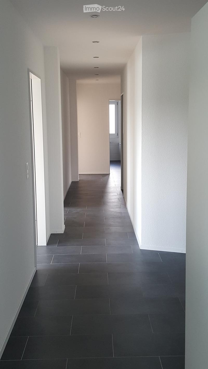 Clean, modern hallway with dark tiled flooring and white walls, featuring recessed ceiling lighting and several doors leading to other rooms.