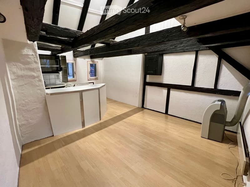 An attic room with exposed wooden beams, white plaster walls, and wooden flooring. The room is empty, with no furniture or equipment visible.