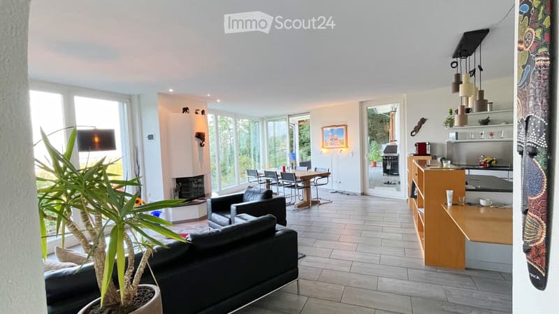 Open-plan living and dining area with large windows, modern furniture, and a kitchen island.