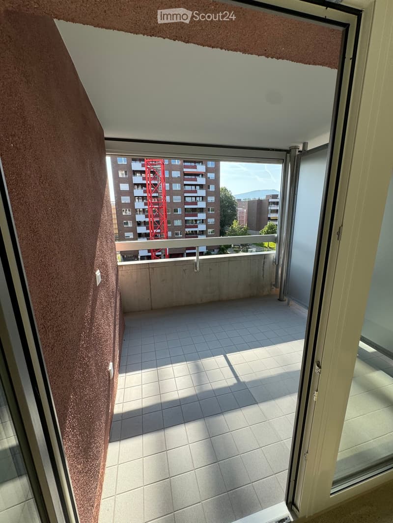 Balcony with tiled floor, open sliding doors, and a view of a residential building and surrounding area.