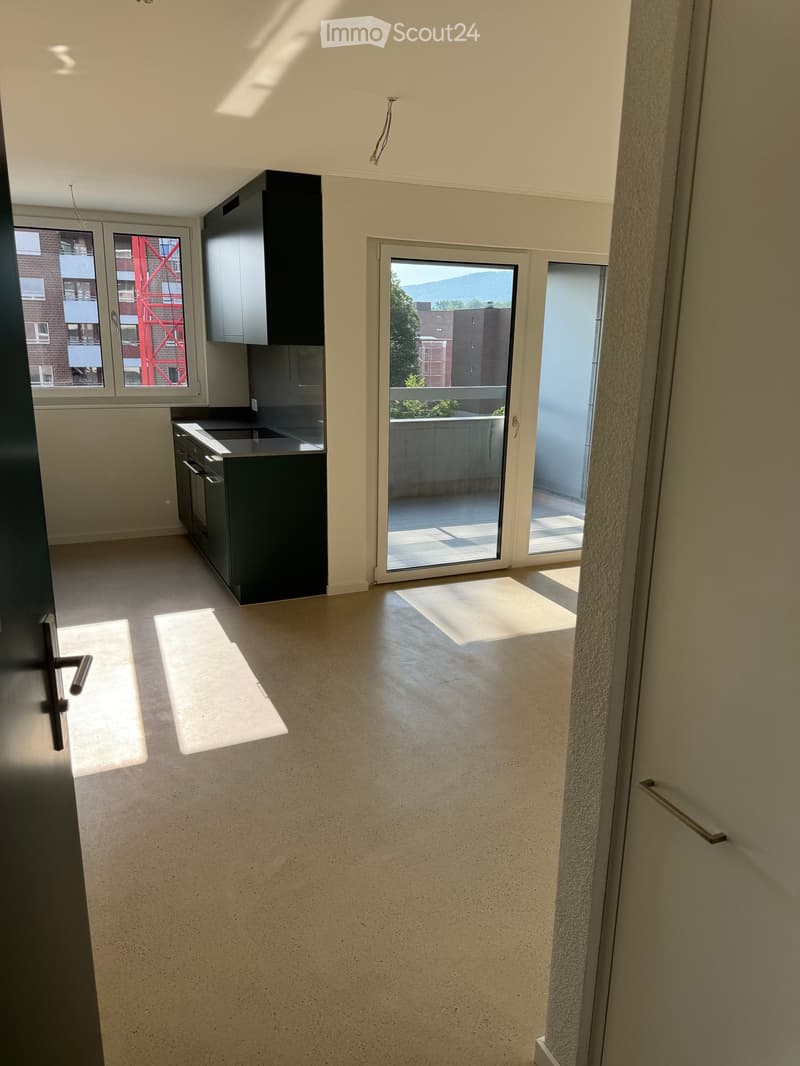 Empty kitchen with modern cabinets, stainless steel appliances, and large windows opening to a balcony.