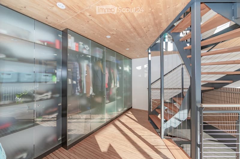 Modern hallway with wooden flooring, glass wardrobe, and a staircase with wooden steps and metal railing.