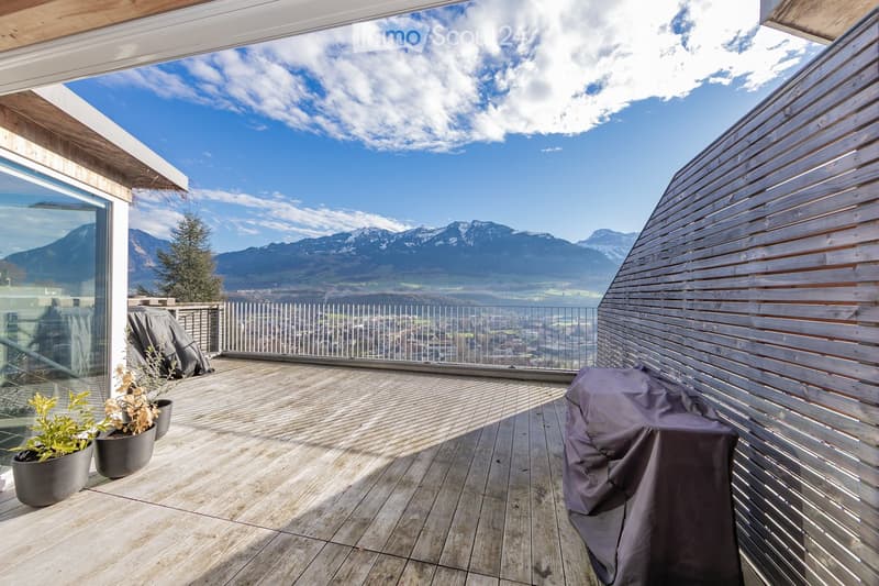 Wooden deck terrace with a panoramic mountain view, covered seating area, and potted plants.
