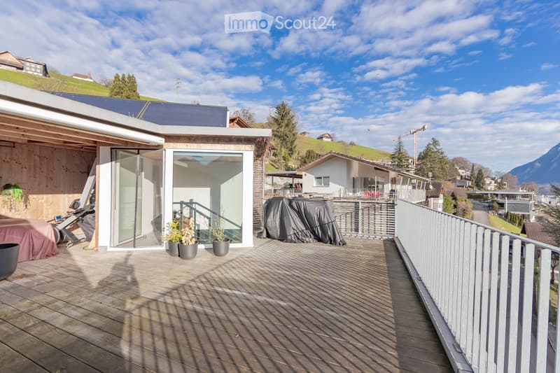 Wooden deck with metal railing, potted plants, covered furniture, and a view of the surrounding landscape and mountains.