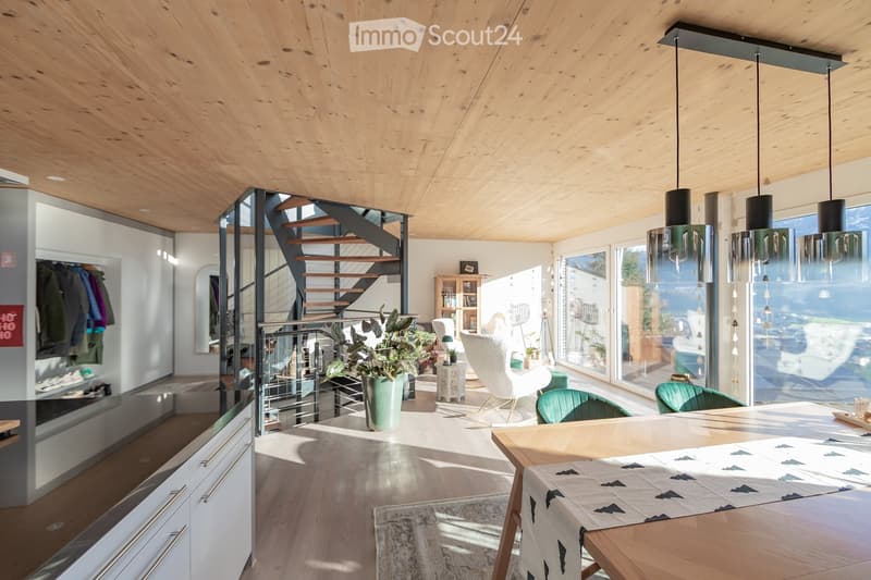 Open-plan living and dining area with wooden ceiling, pendant lights, modern furniture, and large windows offering a view.