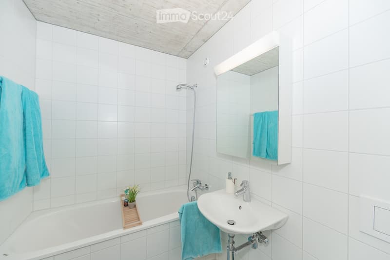 Modern bathroom with white tiled walls and ceiling, featuring a bathtub, sink, mirror, and towel.