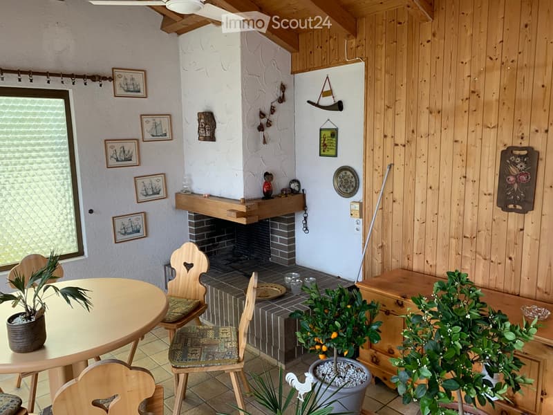 Cozy living room with wooden beams, fireplace, round table, chairs, and potted plants.