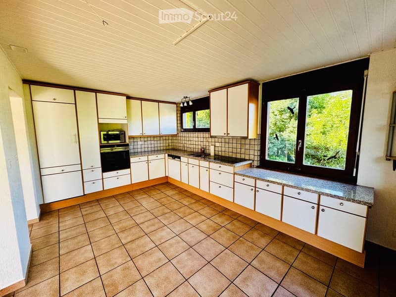 Bright kitchen with white cabinets, granite countertops, tiled floor, and large windows overlooking greenery.