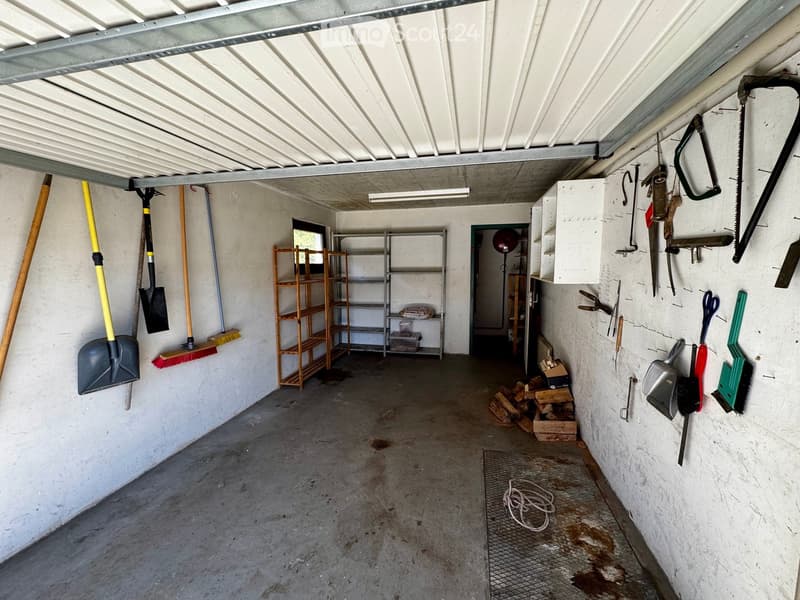 Empty garage with concrete floor, white walls, metal shelving, and various tools and equipment hanging on the walls.