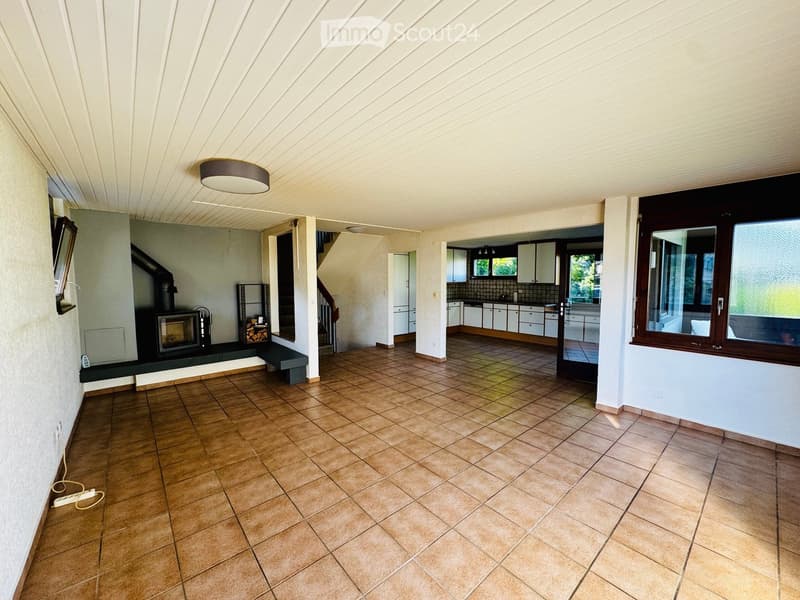 Open-plan living and dining area with tiled flooring, fireplace, bench, and visible kitchen area with cabinets.