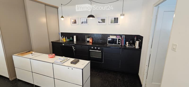 Modern kitchen with black countertops, white cabinets, and stainless steel appliances. Features an oven, microwave, coffee maker, and a small table with books and a decorative box.