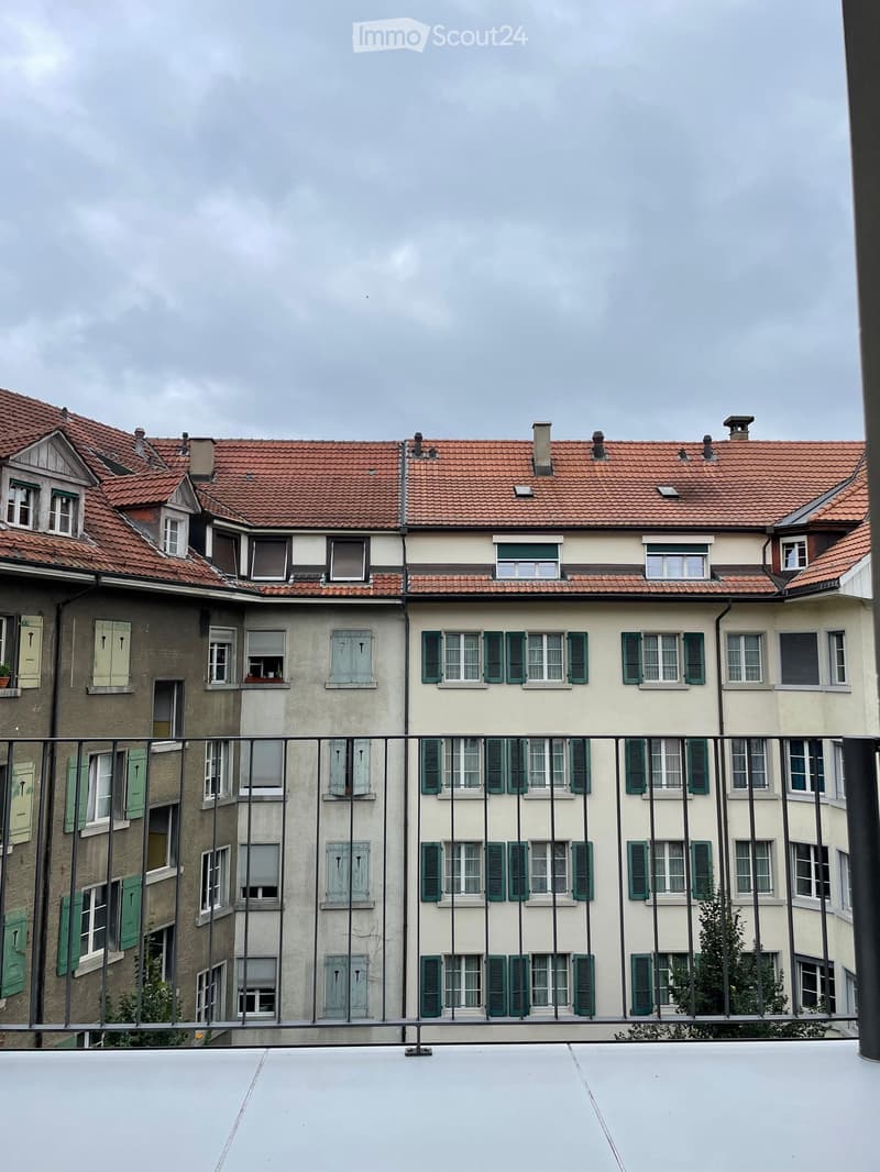 Multi-story residential building with red-tiled roof, multiple windows with green shutters, and visible balconies.