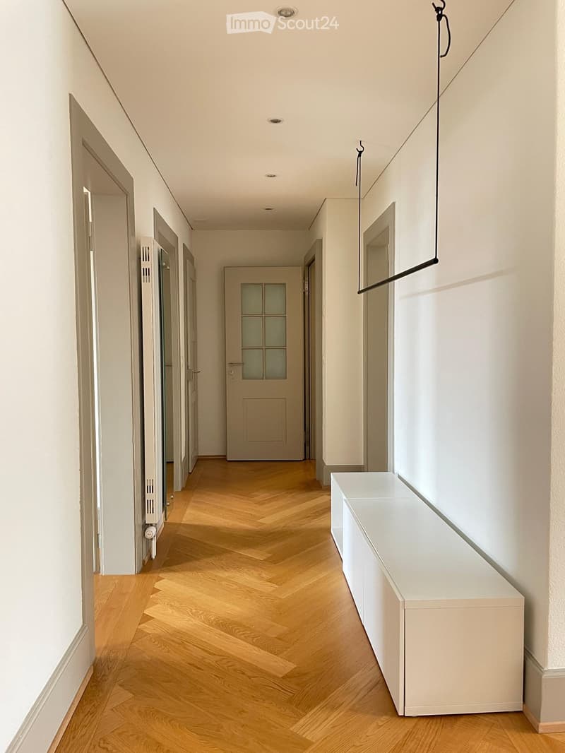 Modern hallway with herringbone wooden flooring, white walls, several doors, and a built-in white bench on the right side.