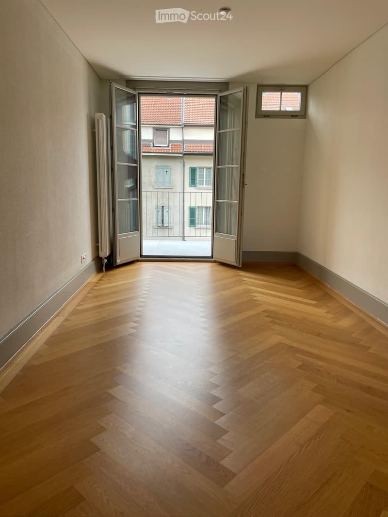 Empty room with wooden flooring, large open doorway leading to a balcony, and visible radiator on the left wall.