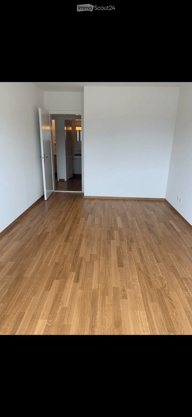Empty room with light wooden flooring and white walls, featuring an open doorway leading to another room.