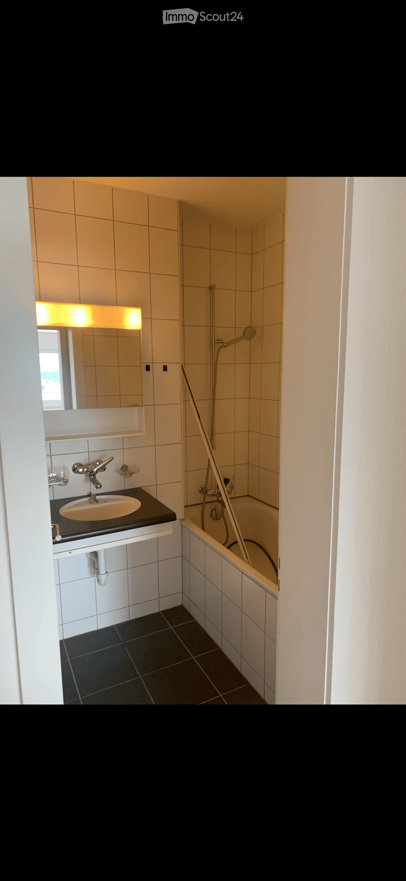Modern bathroom with a white tiled wall, black countertop sink, mirror with built-in lighting, and a bathtub with a handheld showerhead.