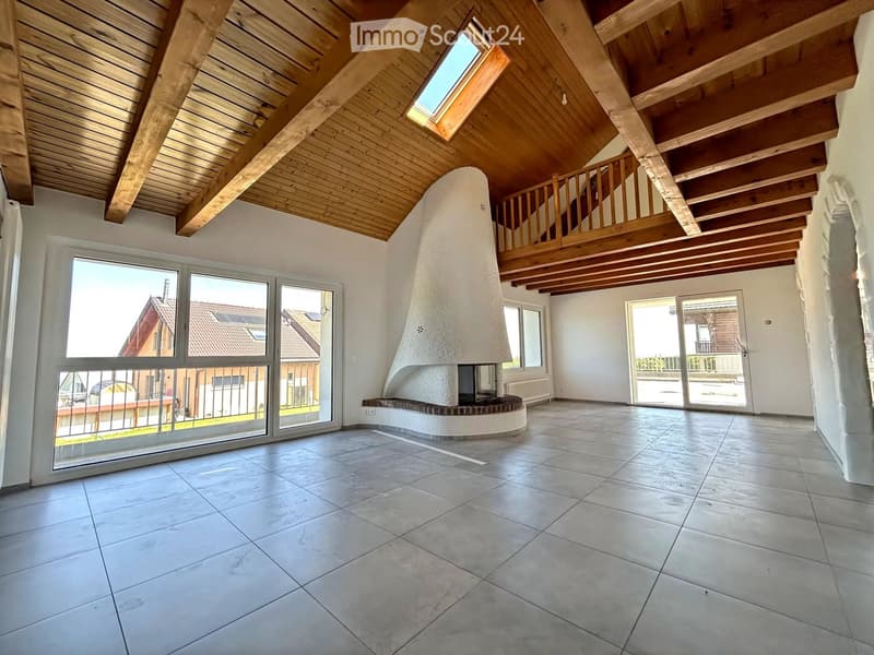Empty room with exposed wooden ceiling beams, skylight, large windows, and a built-in fireplace with a bench seating area.