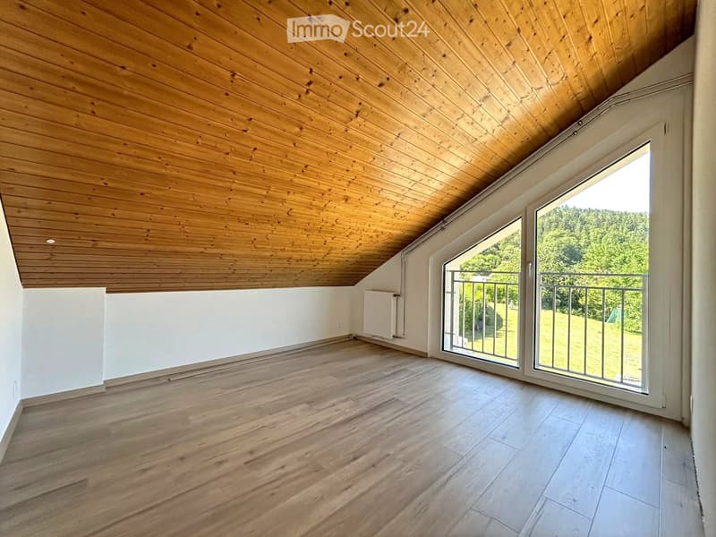 Empty room with wooden floor, white walls, and large sliding glass doors leading to a balcony with a scenic view of greenery.