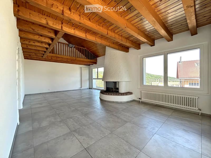 Open-plan living space with exposed wooden beams, tiled floor, built-in fireplace, large windows, and a staircase leading to an upper level.