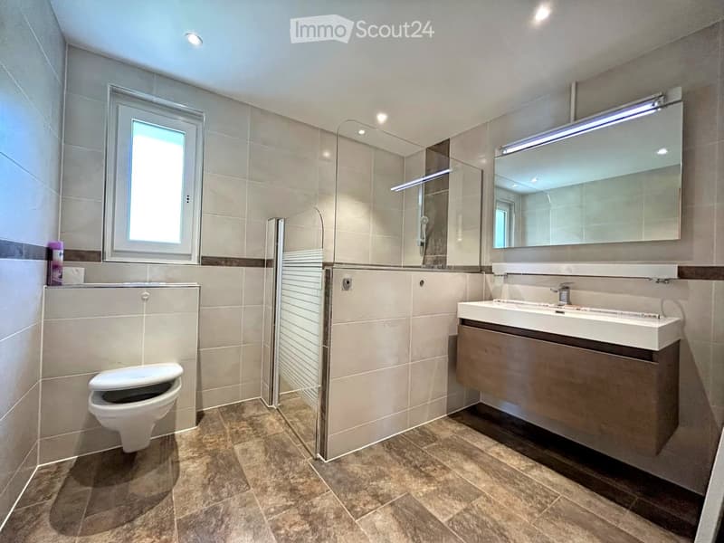 Modern bathroom with beige tiles, a toilet, a sink with a mirror, and a glass-enclosed shower area.