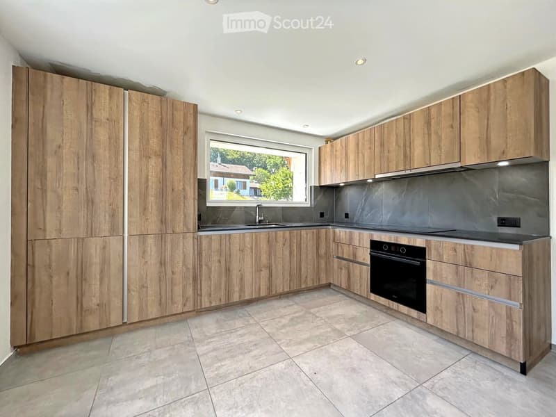 Modern kitchen with light wood cabinets, stainless steel appliances, and a large window overlooking a garden.