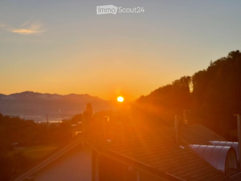 Balcony view at sunset, overlooking a cityscape with mountains in the background.