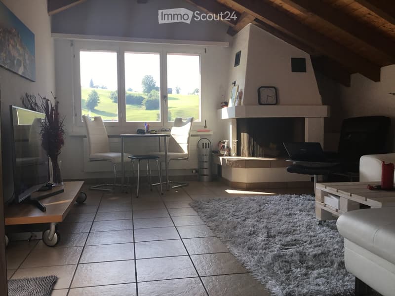 Bright living room with a fireplace, large windows offering a view, a sofa, coffee table, chairs, a laptop, and a screen.