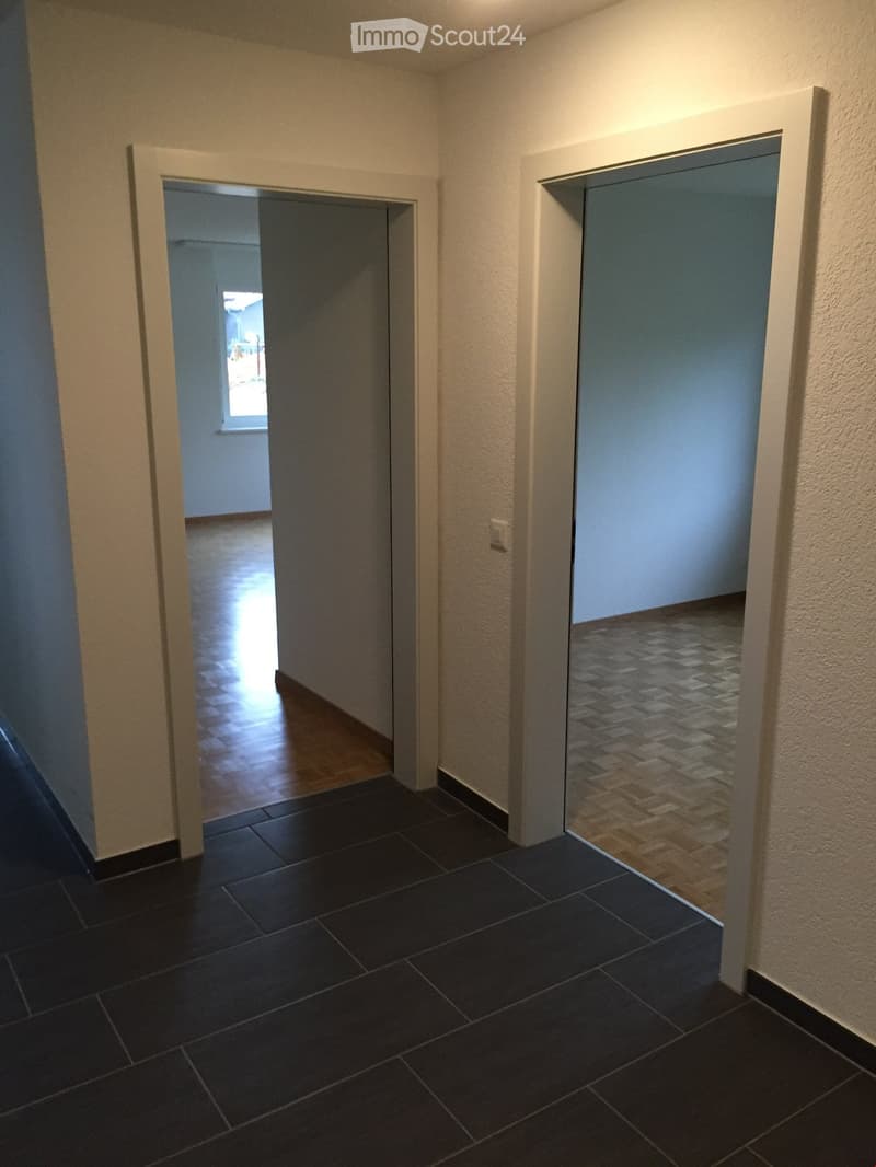 Empty hallway with dark tiled floor, light-colored walls, and two open doors leading to adjacent rooms.