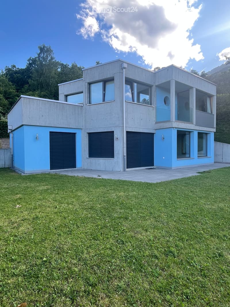 Modern two-story house with concrete and blue exterior, large windows, and multiple garage doors.