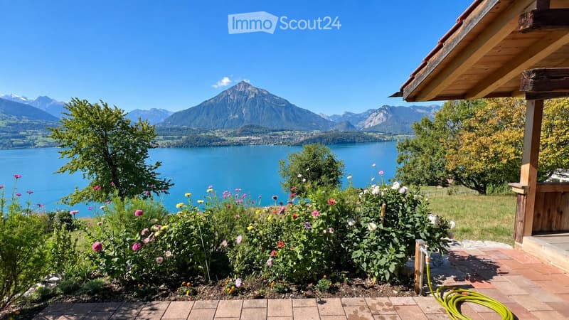 Garden area with colorful flowers, a wooden deck, and a scenic view of a lake and mountains.