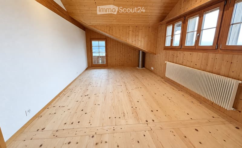 Empty room with wooden floors and walls, large windows, and a radiator. No furniture or equipment present.