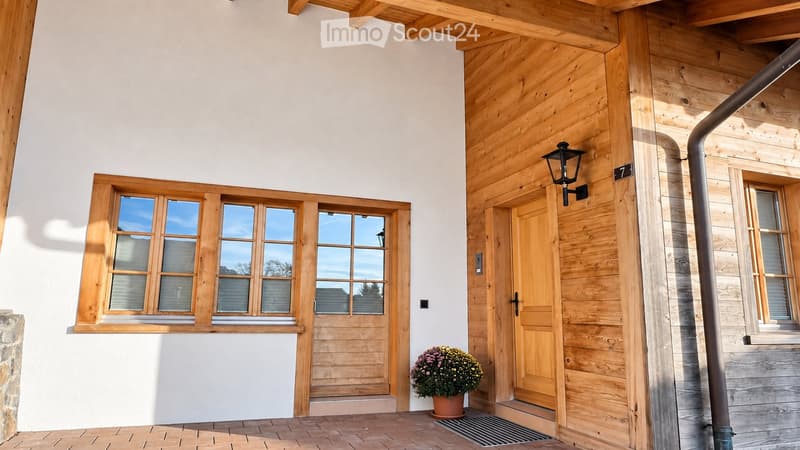 Front view of a modern house with a combination of white and wooden exterior walls, large windows, and a wooden front door.