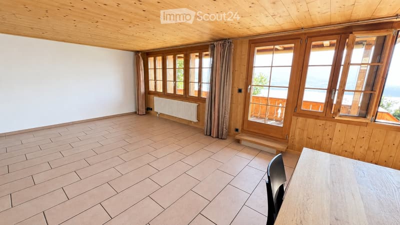 Bright, unfurnished room with wooden walls, large windows, tiled floor, and a small table and chair.