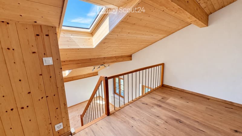 Spacious hallway with wooden flooring, white walls, and a wooden staircase leading to an upper level. Features a skylight and modern lighting fixtures.