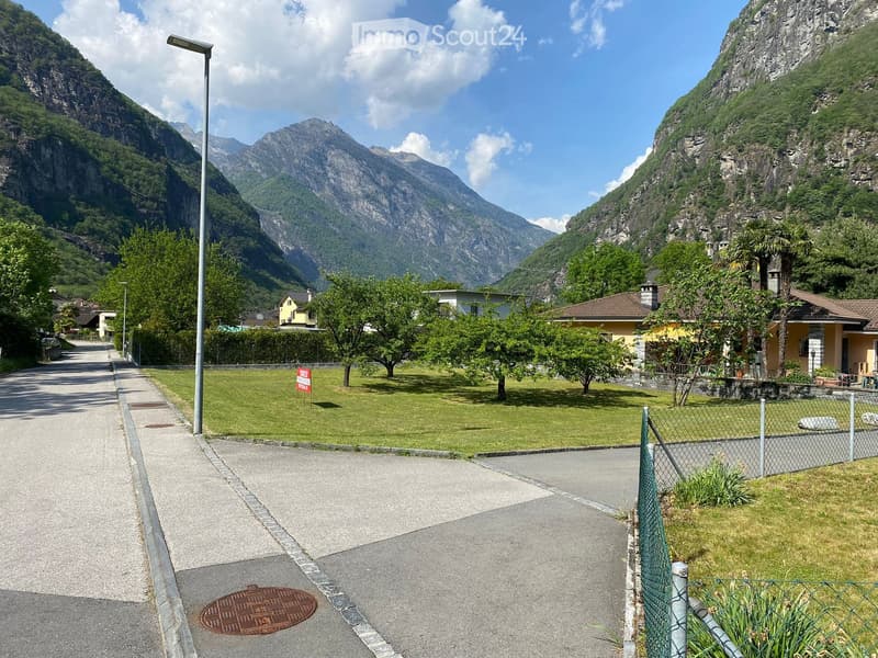 A scenic outdoor area with a paved road, grassy lawn, trees, and distant mountain views.