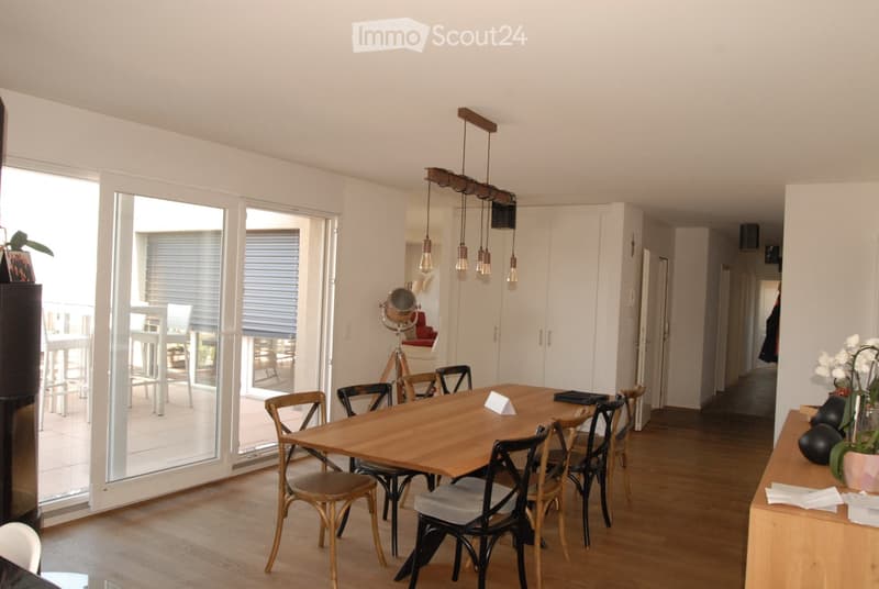 Bright, open dining area with a wooden dining table surrounded by chairs, a potted plant on a sideboard, and large glass doors leading to a balcony.