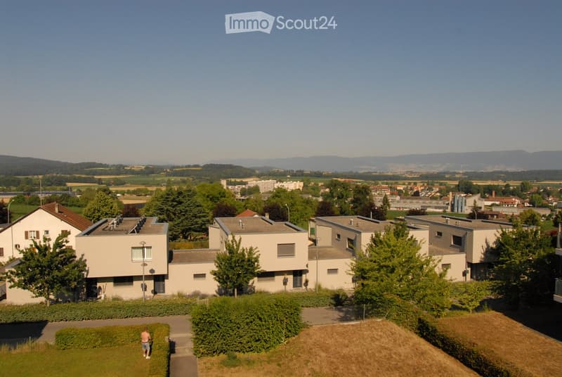 Aerial view of a residential area with multiple modern houses, surrounded by greenery and distant hills.