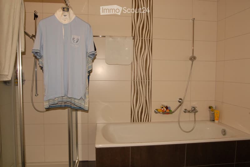 Bathroom with a bathtub, shower hose, towel hanging on a rack, a cup, and a toy on the edge of the tub.