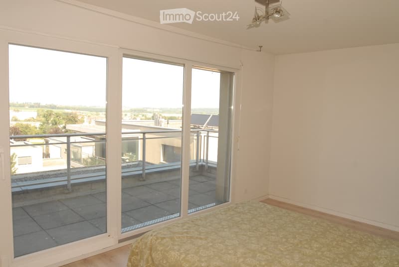 Bright bedroom with wooden flooring, large sliding glass doors opening to a balcony, and a neatly made bed.