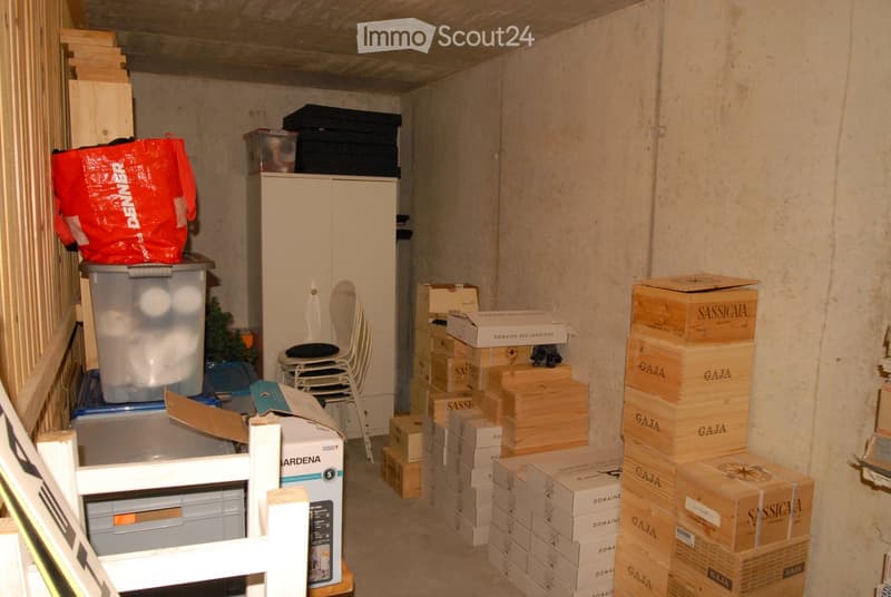 A cluttered storage room with a chair, cabinet, plastic bag, and numerous stacked boxes and crates.