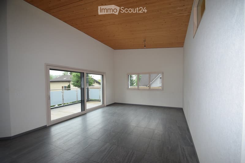 Empty room with white walls, dark grey tiled floor, wooden ceiling, large sliding glass door leading to a balcony, and a window with white frame.