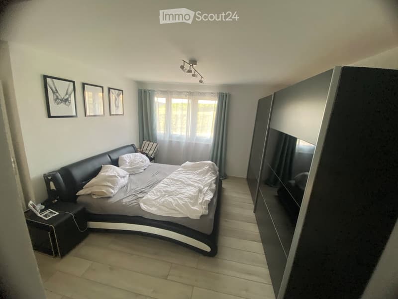 Modern bedroom with a large bed, sofa, mirror, nightstand, and picture frames on the wall.