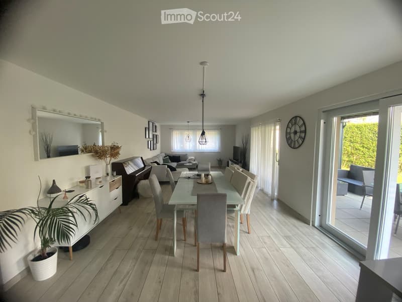 Open-plan living and dining area with light wooden flooring, a sofa, dining table with chairs, a large mirror, and decorative items.