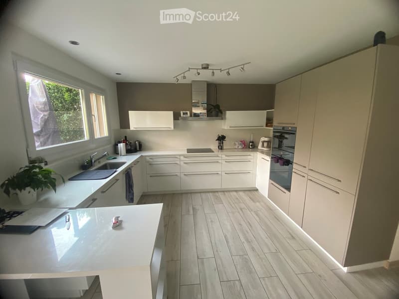 Modern kitchen with white cabinets, wooden flooring, and stainless steel appliances. Features a central island with a sink and a built-in oven and refrigerator.
