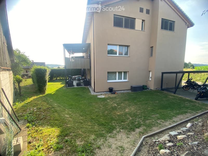 Well-maintained garden with a covered patio area, outdoor furniture, and a motorcycle parked nearby.