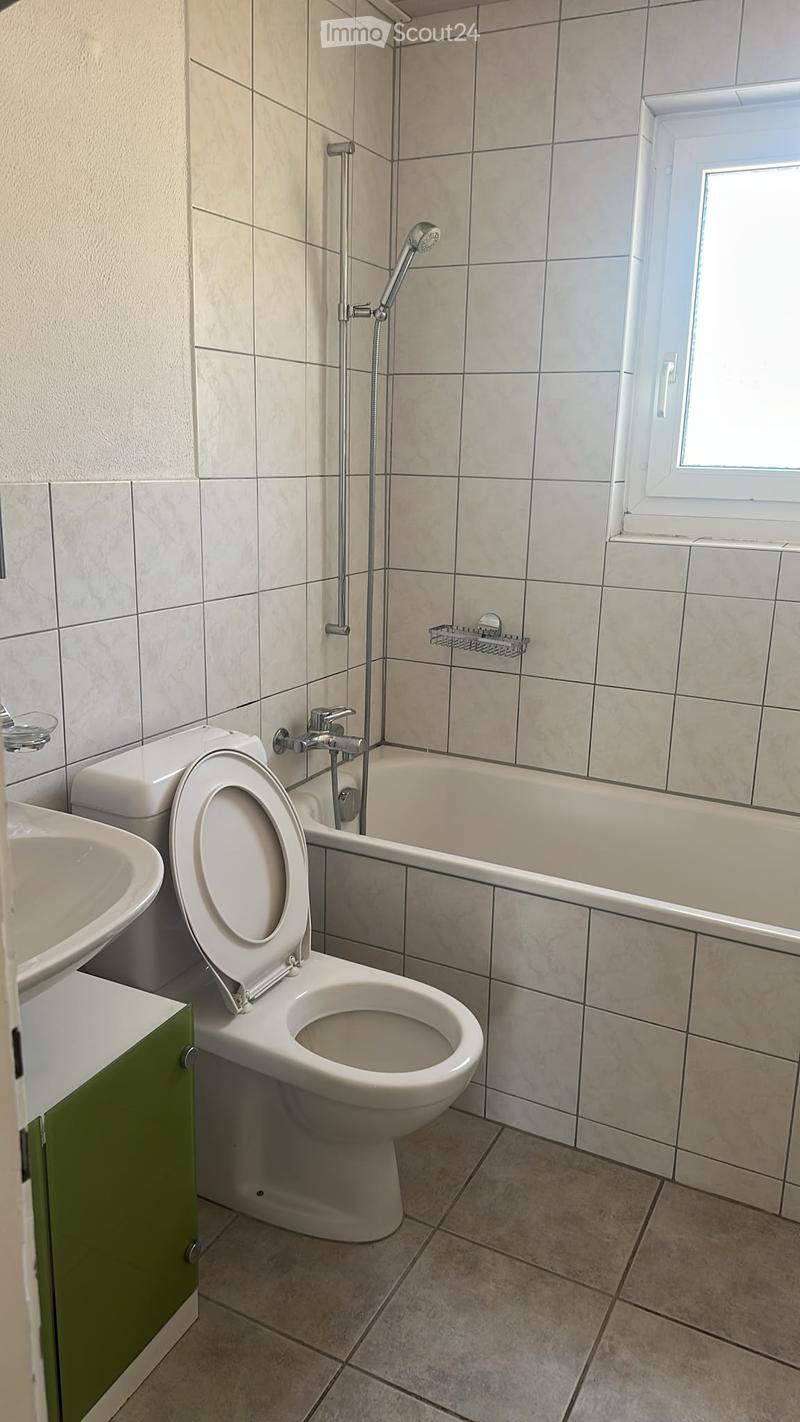 Modern bathroom with beige tiled walls and floor, featuring a toilet, bathtub, sink, and showerhead.