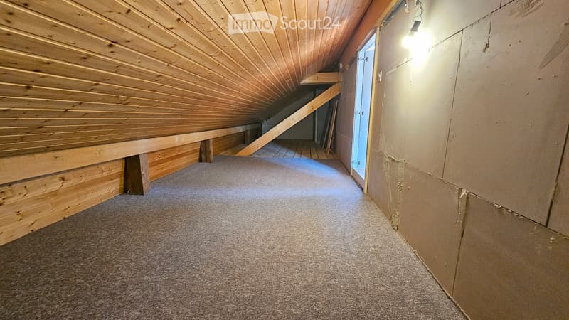 Carpeted hallway with wooden ceiling beams and exposed wooden support beams, leading to an open doorway.