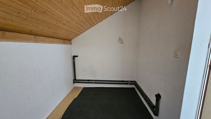 Empty room with white walls, wooden ceiling, and black floor. No furniture or equipment present.