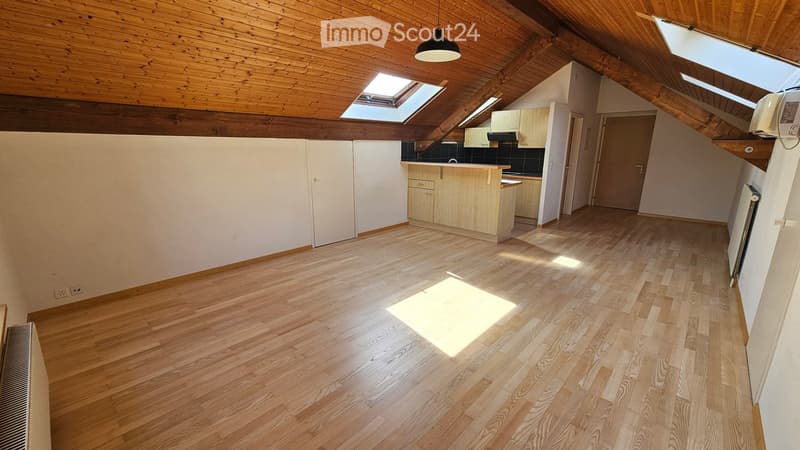 Bright, open attic space with wooden floors, white walls, and skylights. Features a small kitchen area with cabinets and a countertop, and a radiator on the wall.